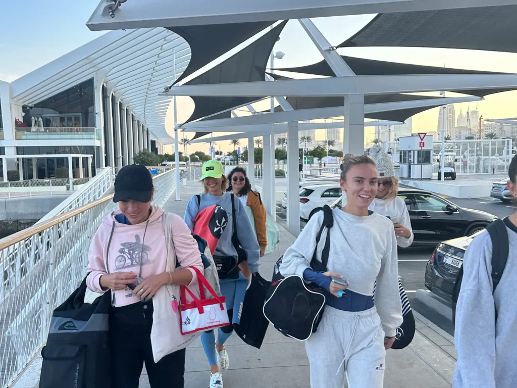 group of girls walking in the marina port holding surf boards